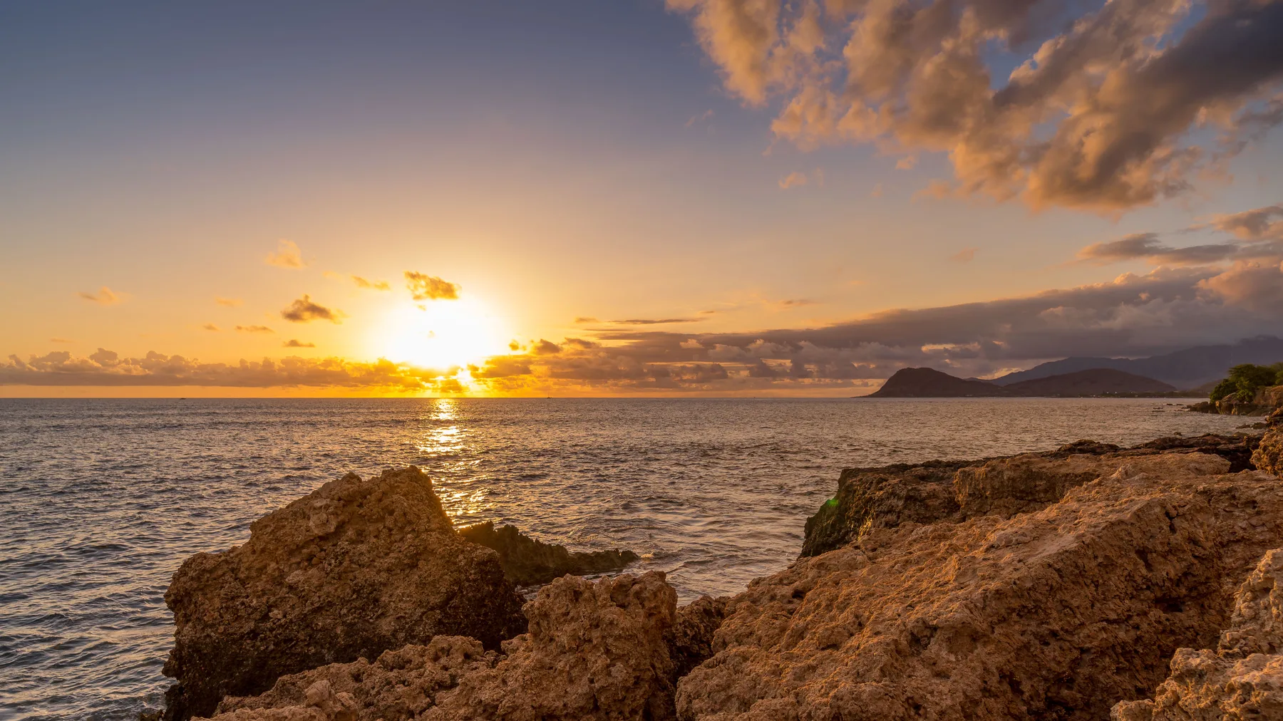 Atardecer sobre el océano, con una costa rocosa en primer plano.
