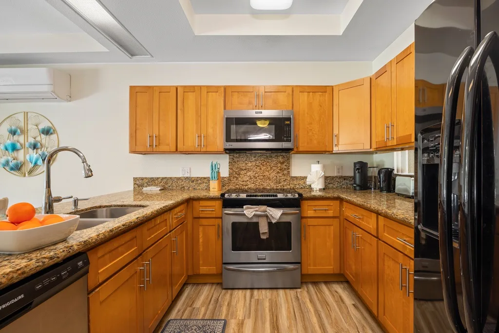 Una cocina con gabinetes de madera, encimeras de granito y electrodomésticos de acero inoxidable.