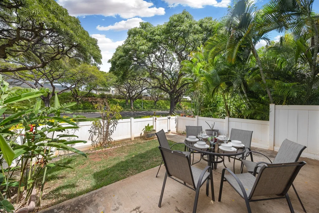 Un patio exterior tiene una mesa de comedor y sillas junto a un jardín.