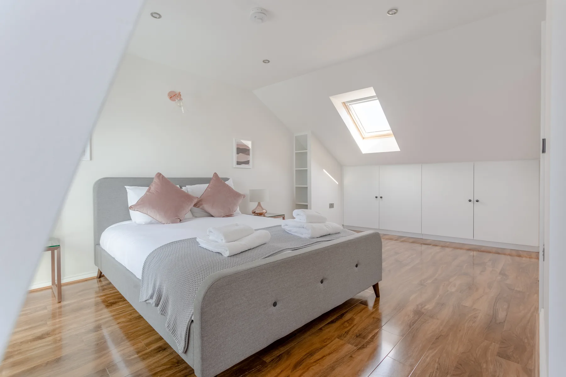 Un dormitorio luminoso con una cama bajo una claraboya y armarios empotrados.