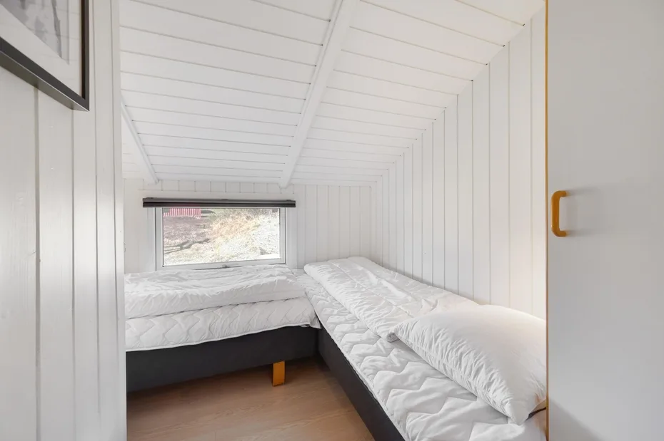 A compact sleeping area with two beds beneath a sloped white-paneled ceiling.
