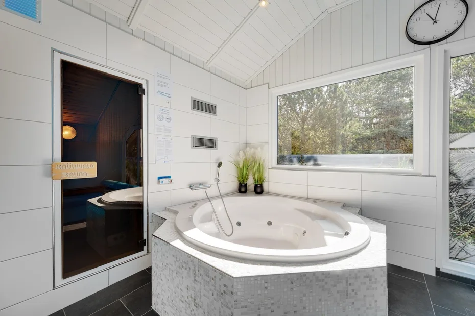 A bright bathroom features a large corner bathtub beneath a wide window.