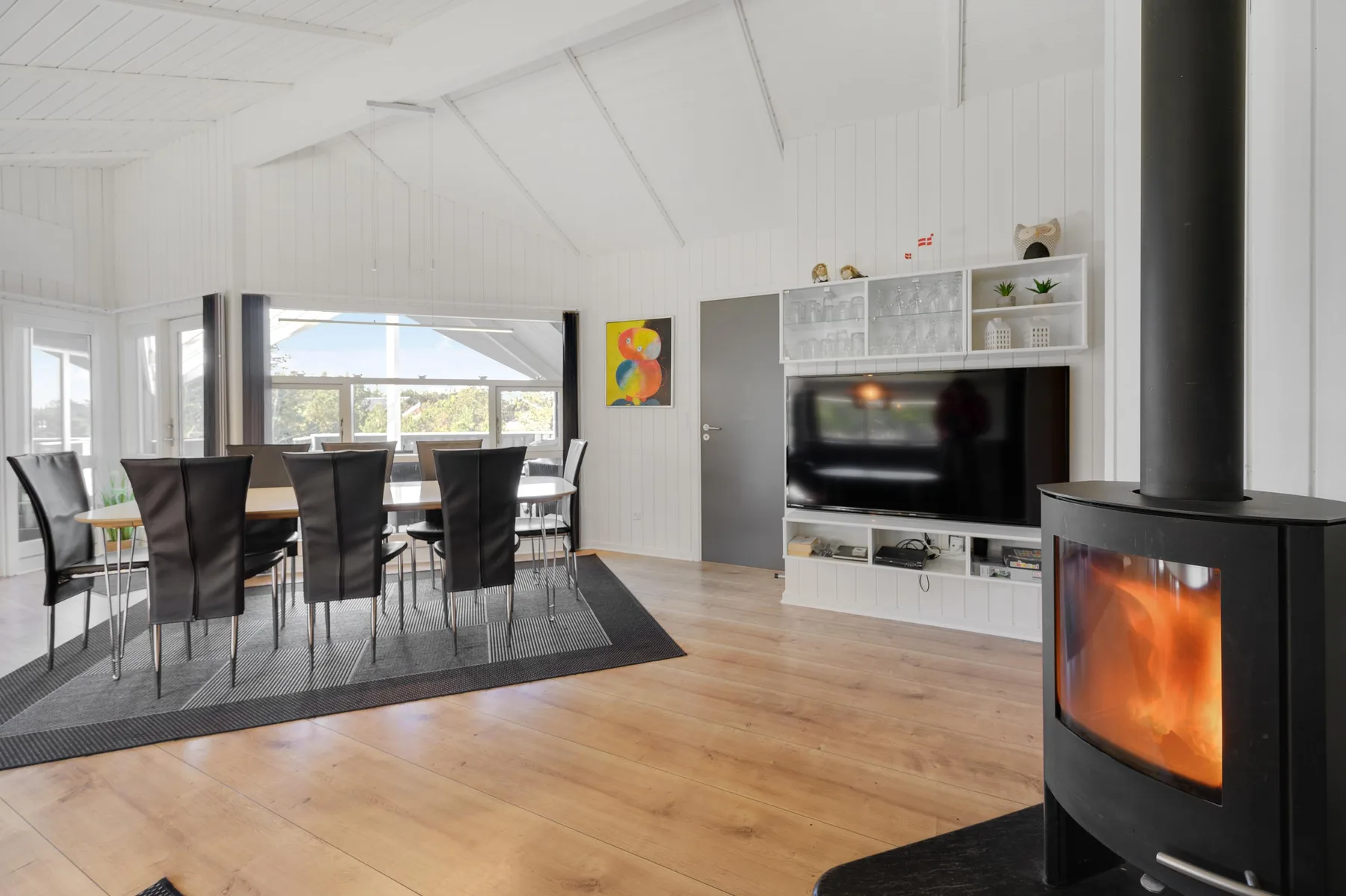 A bright living and dining area with a television and a lit wood stove.