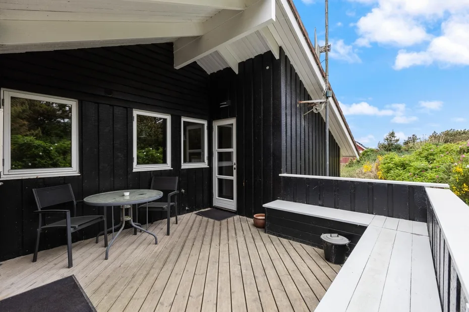An outdoor deck with seating beside a black-sided building.