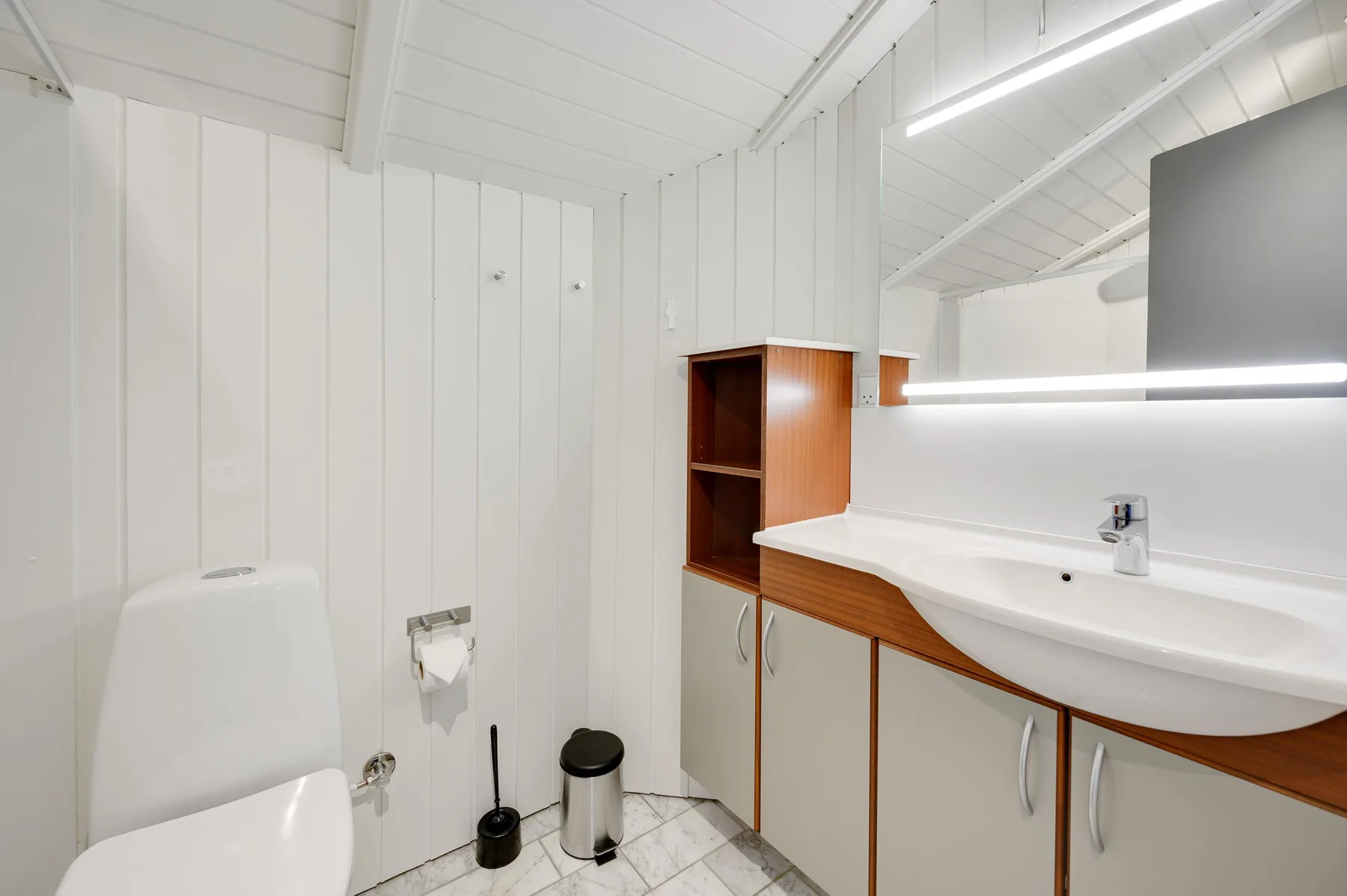 A bright bathroom with a wide sink and mirrored wall.
