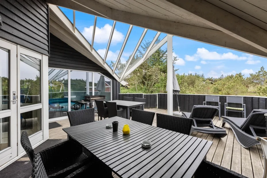 An outdoor deck features a dark dining table and several lounge chairs.