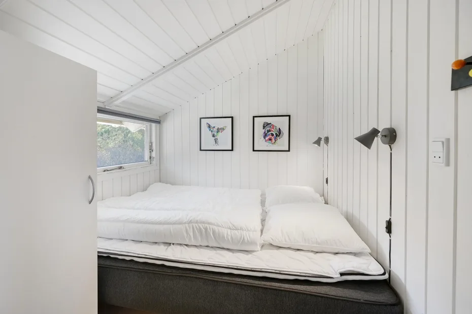 A bedroom with white bedding, framed artwork, and wall-mounted lighting.