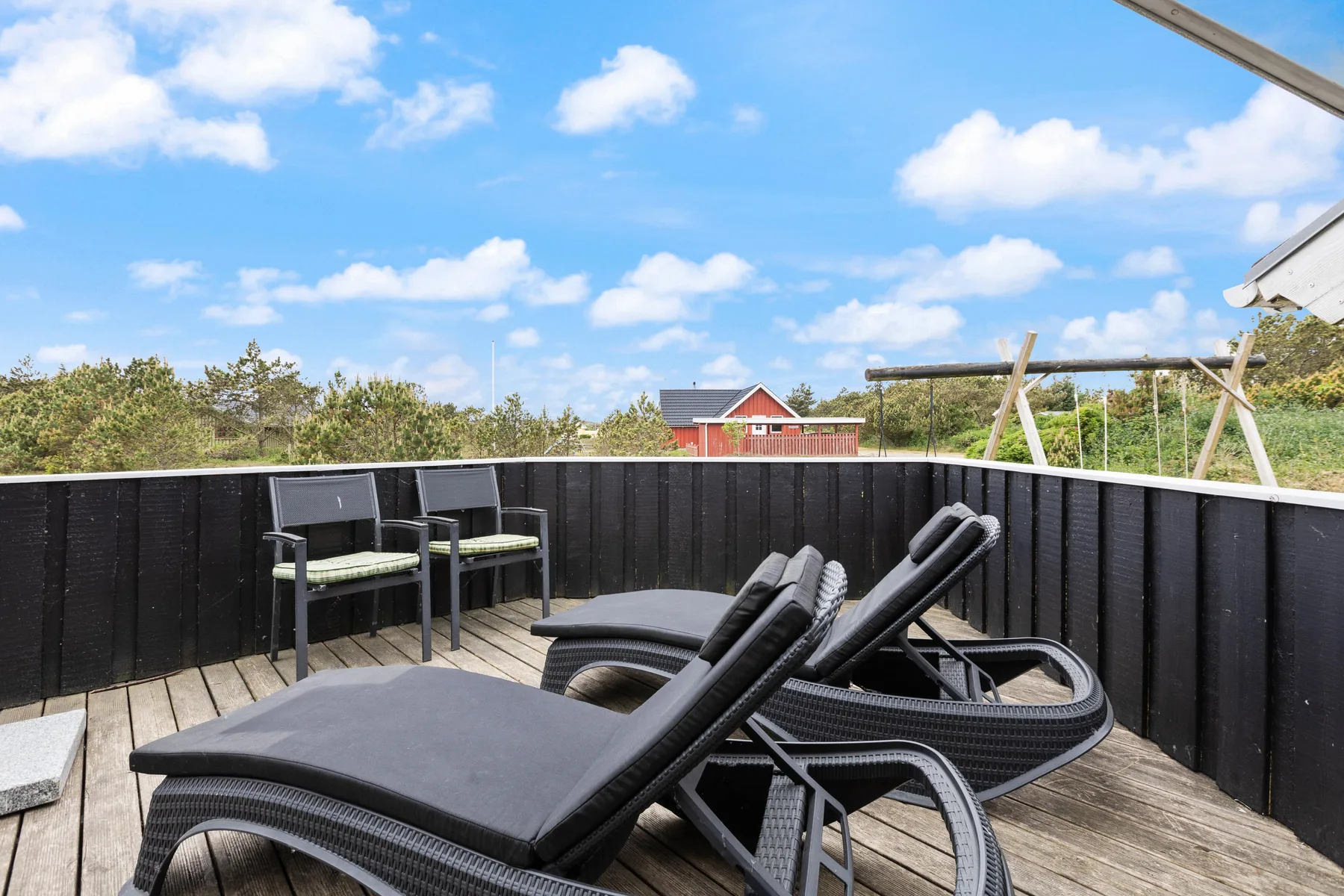 A wooden deck has reclining outdoor seating beside a dark railing.