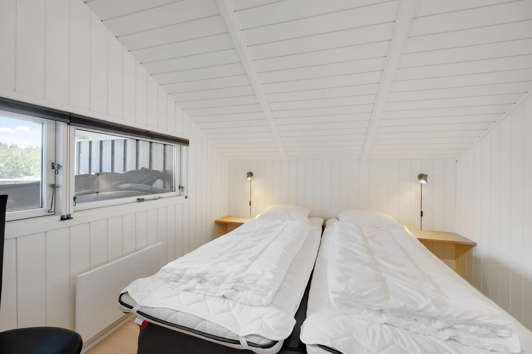 A bright bedroom with two beds beneath a sloped white ceiling.