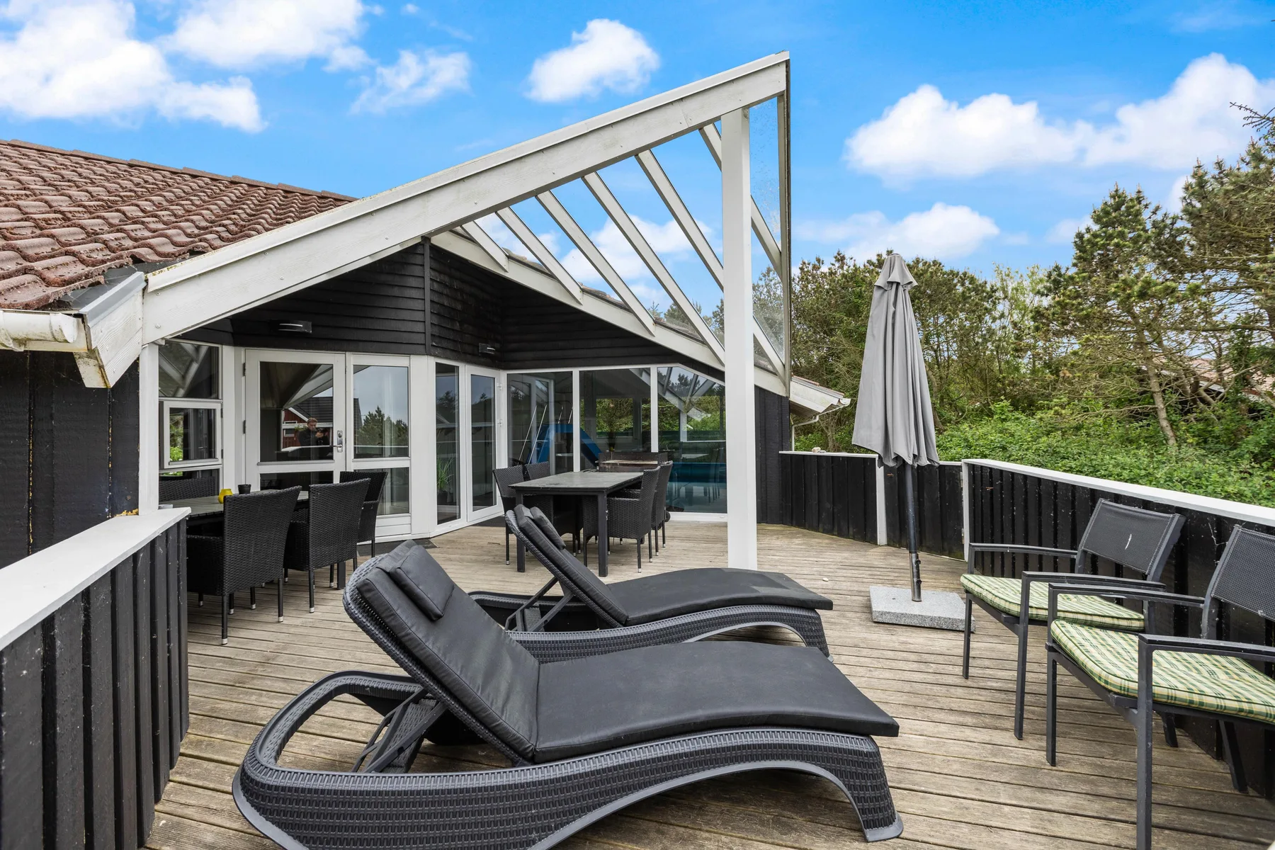 A sunny outdoor deck with lounge seating beside a dark house.