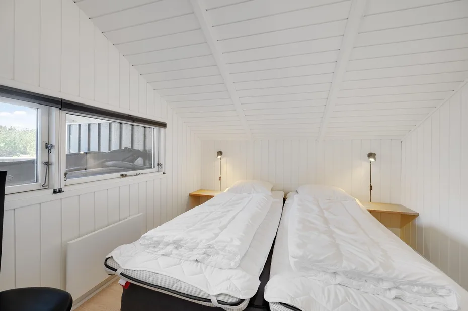 A bright bedroom with two beds beneath a sloped white ceiling.