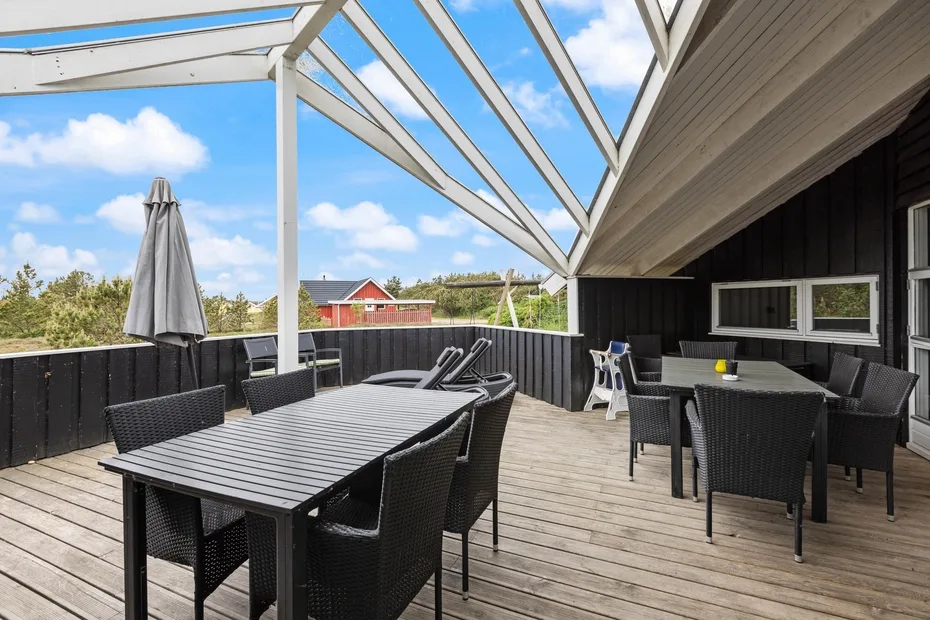 A covered outdoor dining area with dark tables and seating on a wooden deck.