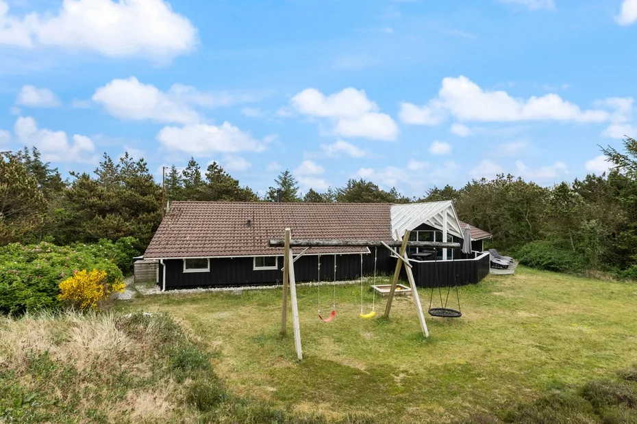 A long, low building stands beside a grassy yard and a wooden swing set.