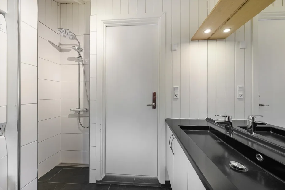 A bathroom with a shower, a closed door, and a long black countertop.