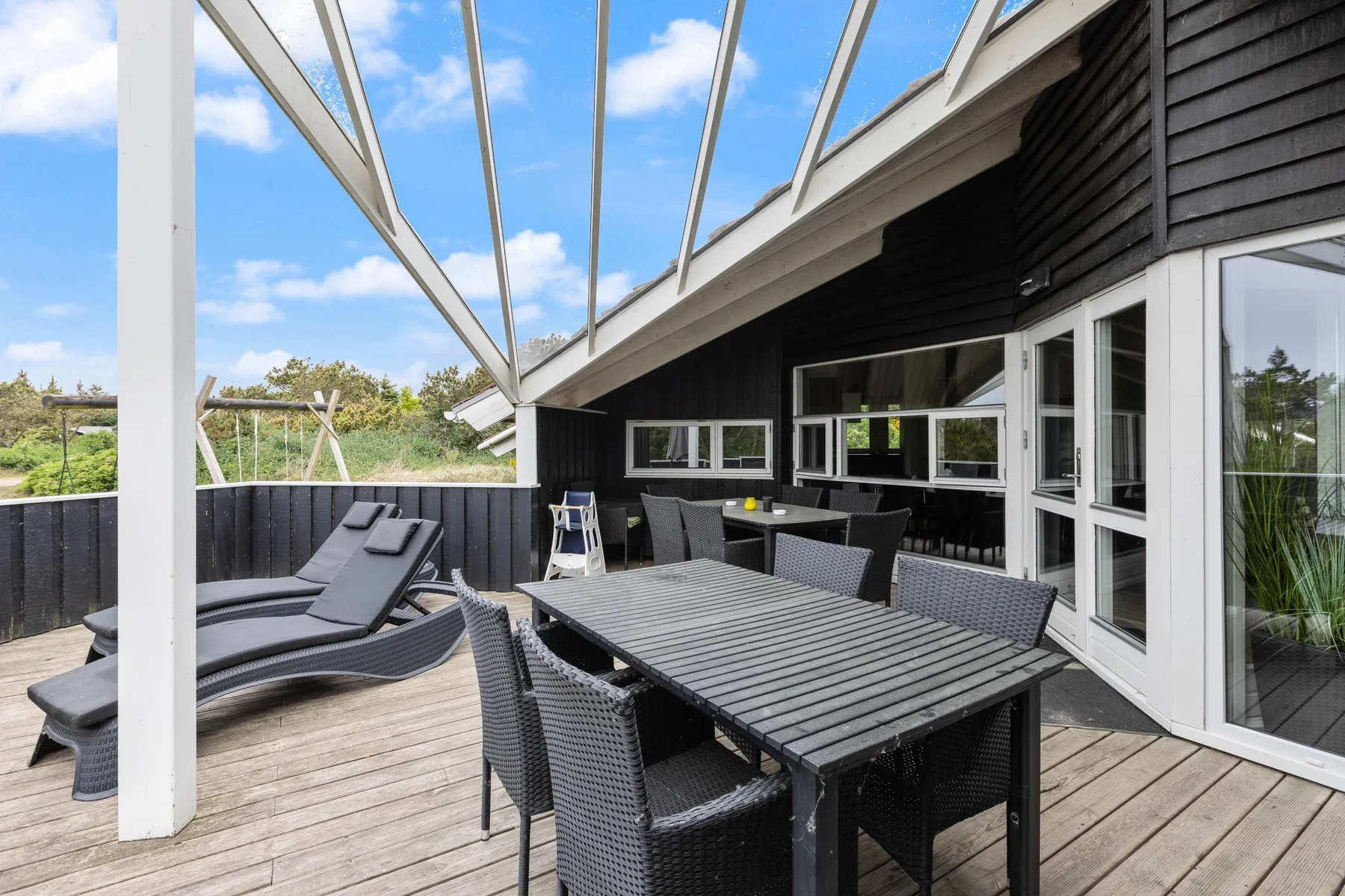 A covered outdoor dining area with dark seating and a long table.