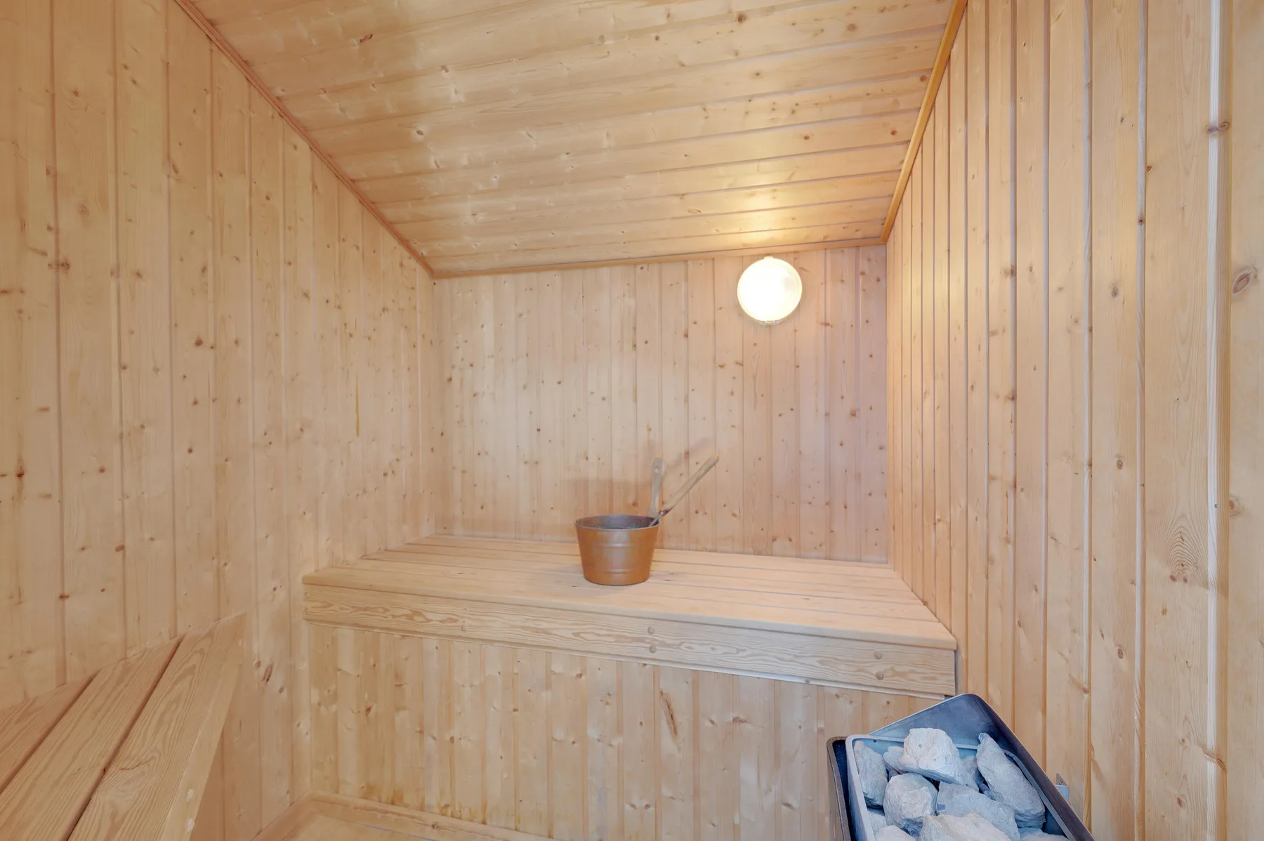 A wood-paneled sauna with a raised bench and a small pail.