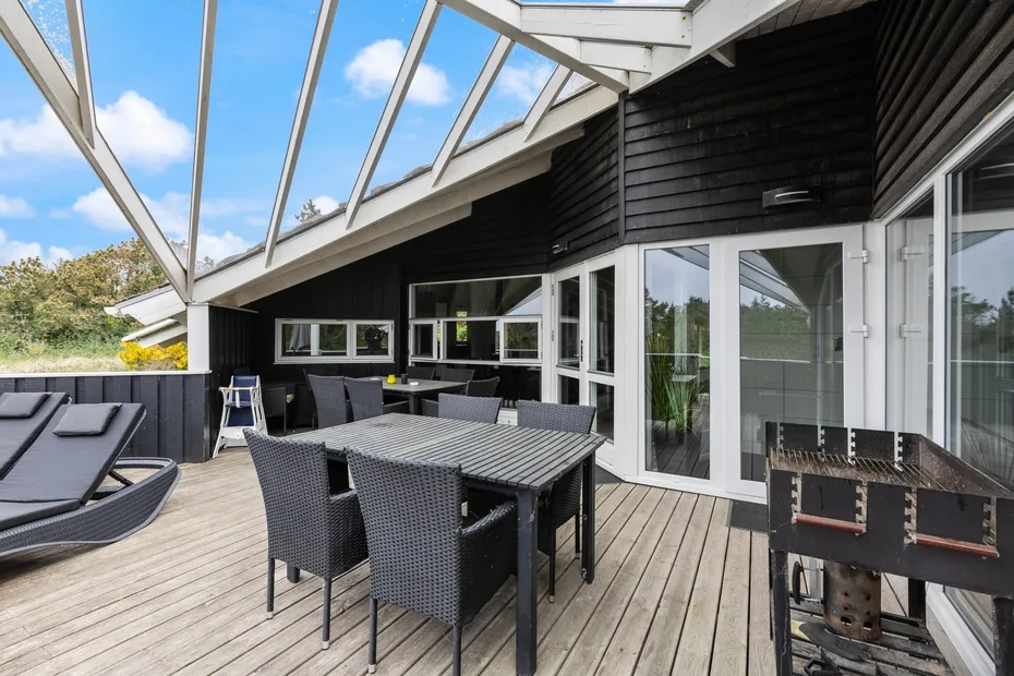 An outdoor deck with dining seating, loungers, and a grill beside the house.