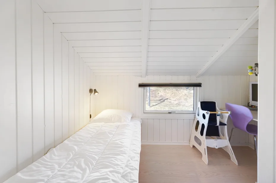 A bright bedroom with a bed, a window, and a small desk area.