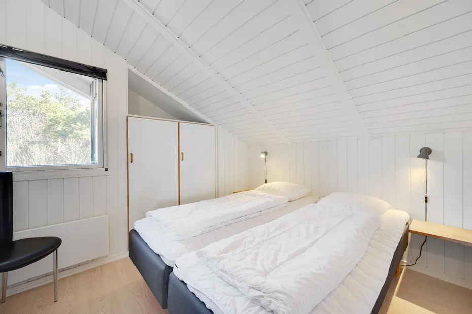 A bright bedroom with two beds beneath a sloped white ceiling.