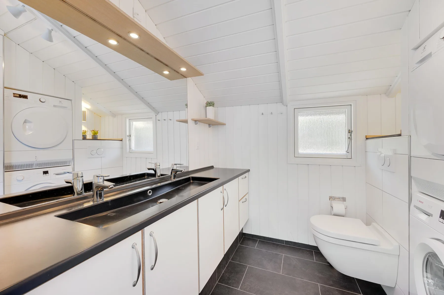 A bright bathroom with a long vanity, sink, and toilet.