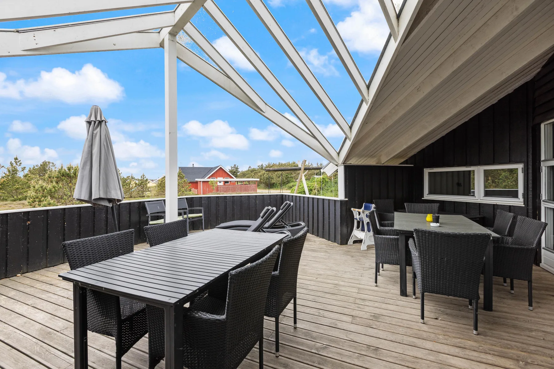 A spacious outdoor deck has dining tables, seating, and an overhead pergola.