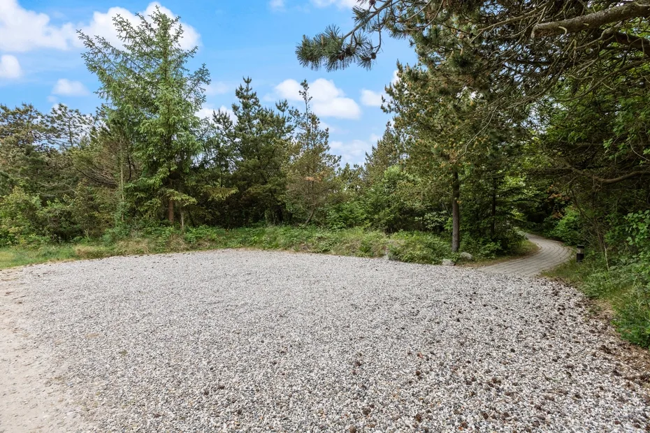 A gravel clearing surrounded by trees, with a narrow path curving through the greenery.