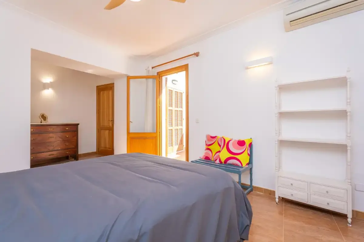 Un dormitorio con cama, cómoda y una puerta abierta a una zona contigua iluminada.
