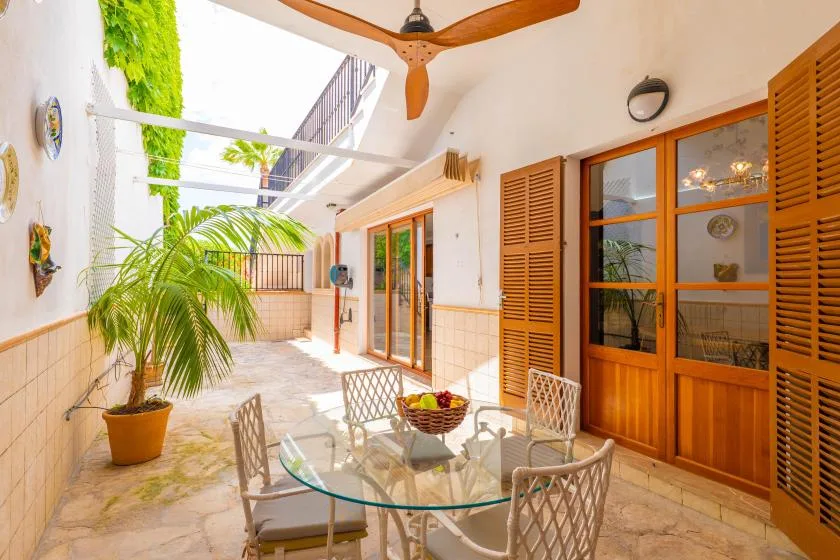 Un patio luminoso con mesa de comedor de vidrio, asientos y puertas de madera.