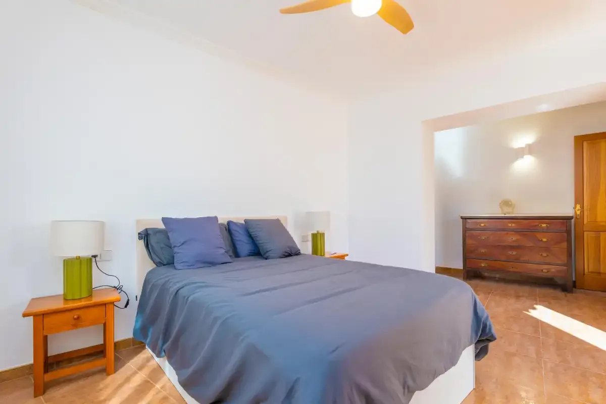 Un dormitorio con una cama vestida con ropa de cama azul y una mesita de noche de madera.