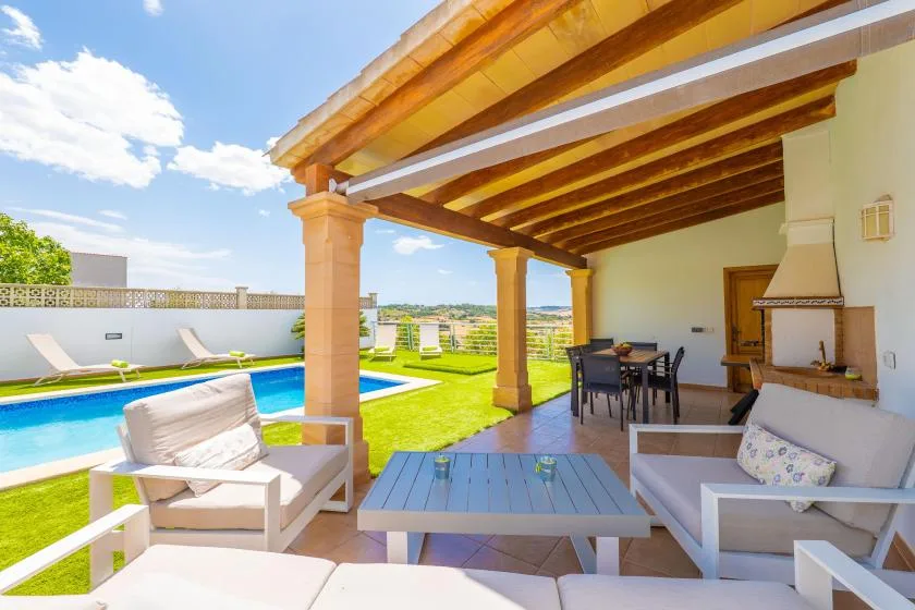 Un patio cubierto con asientos y una mesa da a una piscina y un césped.