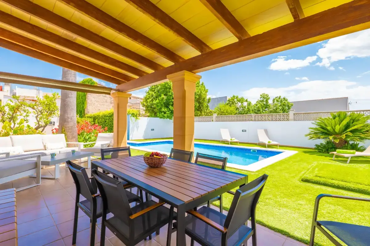 Una zona de comedor exterior cubierta da a una piscina y un césped.