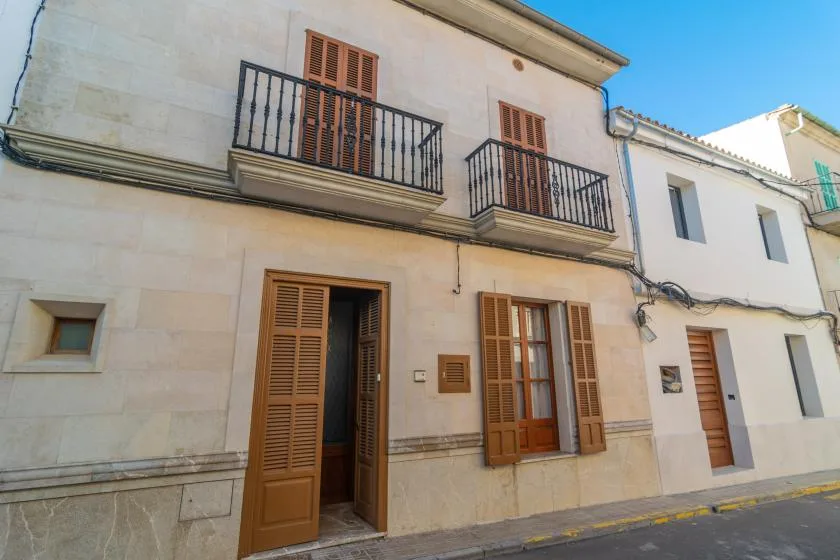 Vista de un edificio claro que da a la calle, con ventanas con contraventanas y pequeños balcones.