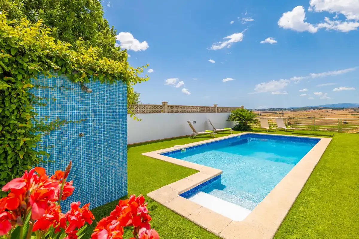 Una piscina al aire libre está rodeada de césped verde y plantas con flores.