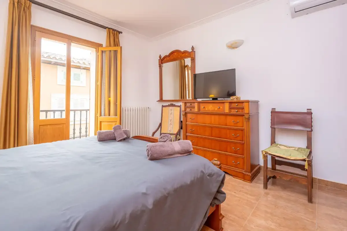Un dormitorio con una cama, una cómoda de madera y puertas al balcón.