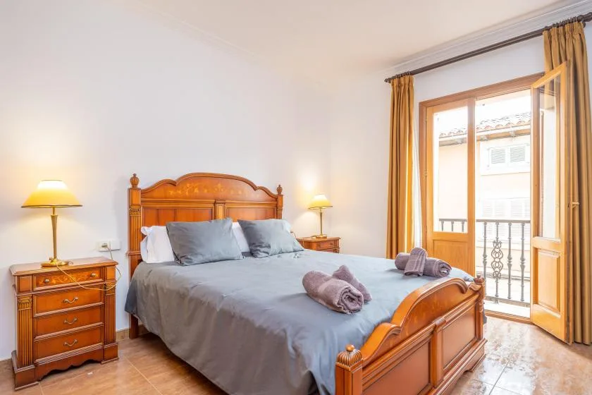 Un dormitorio con una cama de madera, mesas de noche y una puerta abierta al balcón.