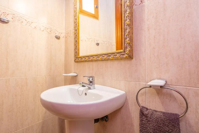 Un baño con paredes revestidas de azulejos, lavabo y espejo decorativo.