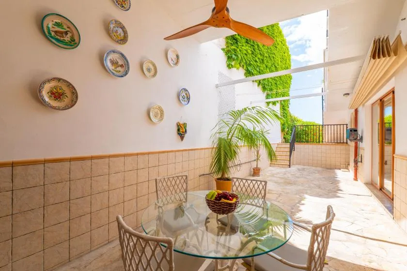 Un luminoso comedor en el patio con una mesa de vidrio y vistas a la vegetación.