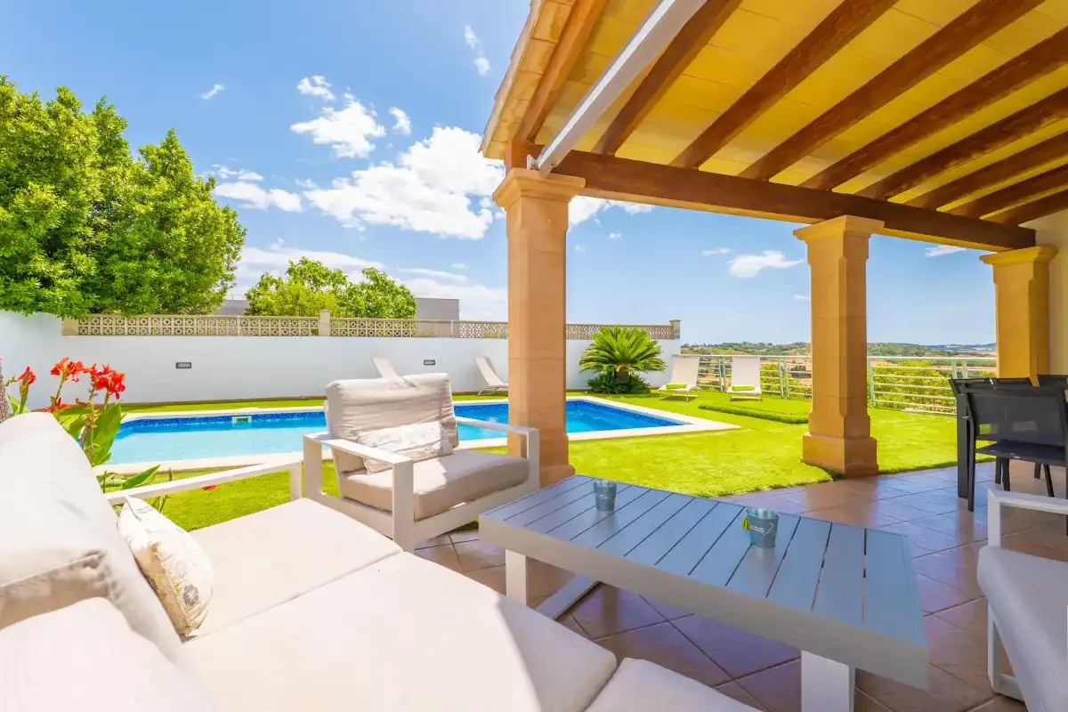 Un patio cubierto con asientos al aire libre da a una piscina y un césped.