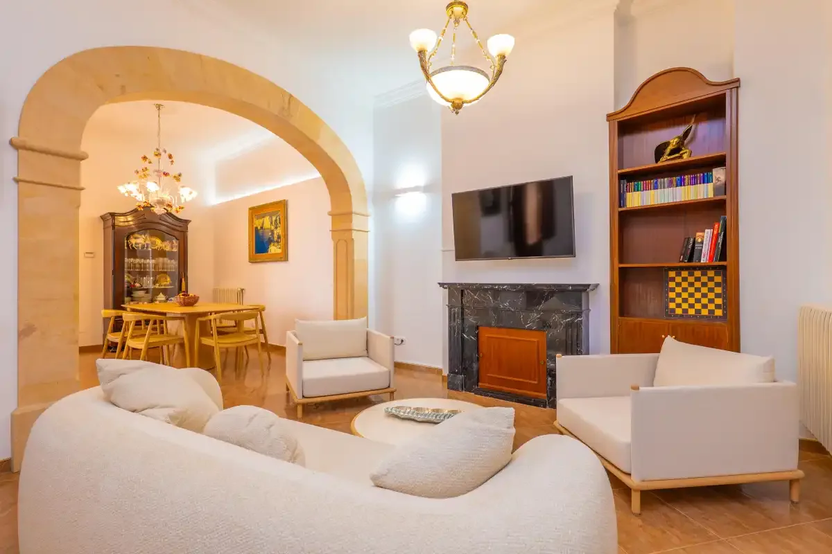 Una sala de estar con asientos, un televisor y un arco que da a un comedor.
