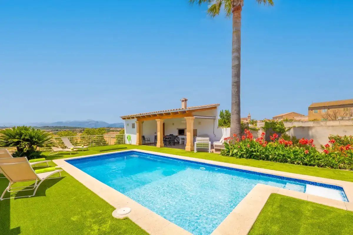 Una piscina exterior está junto a una zona de estar cubierta y un césped ajardinado.