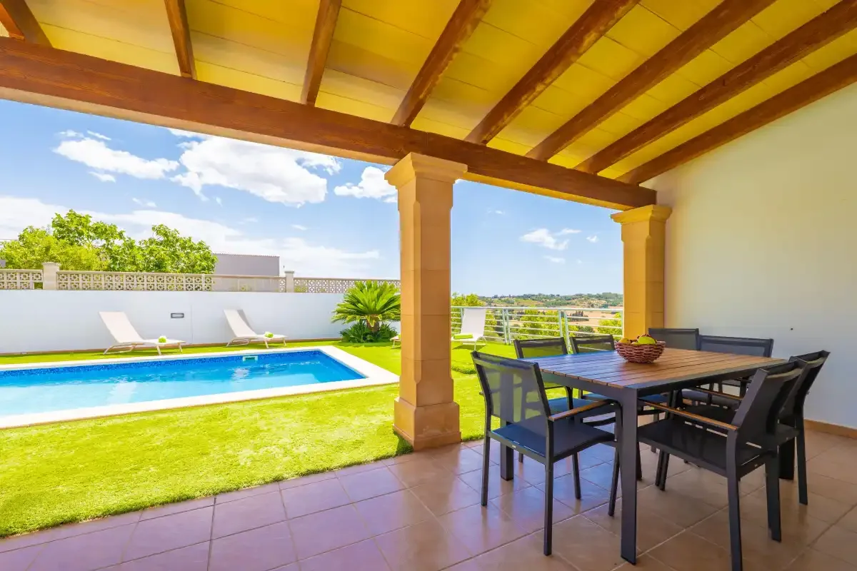 Una zona de comedor exterior cubierta da a una piscina y un césped.