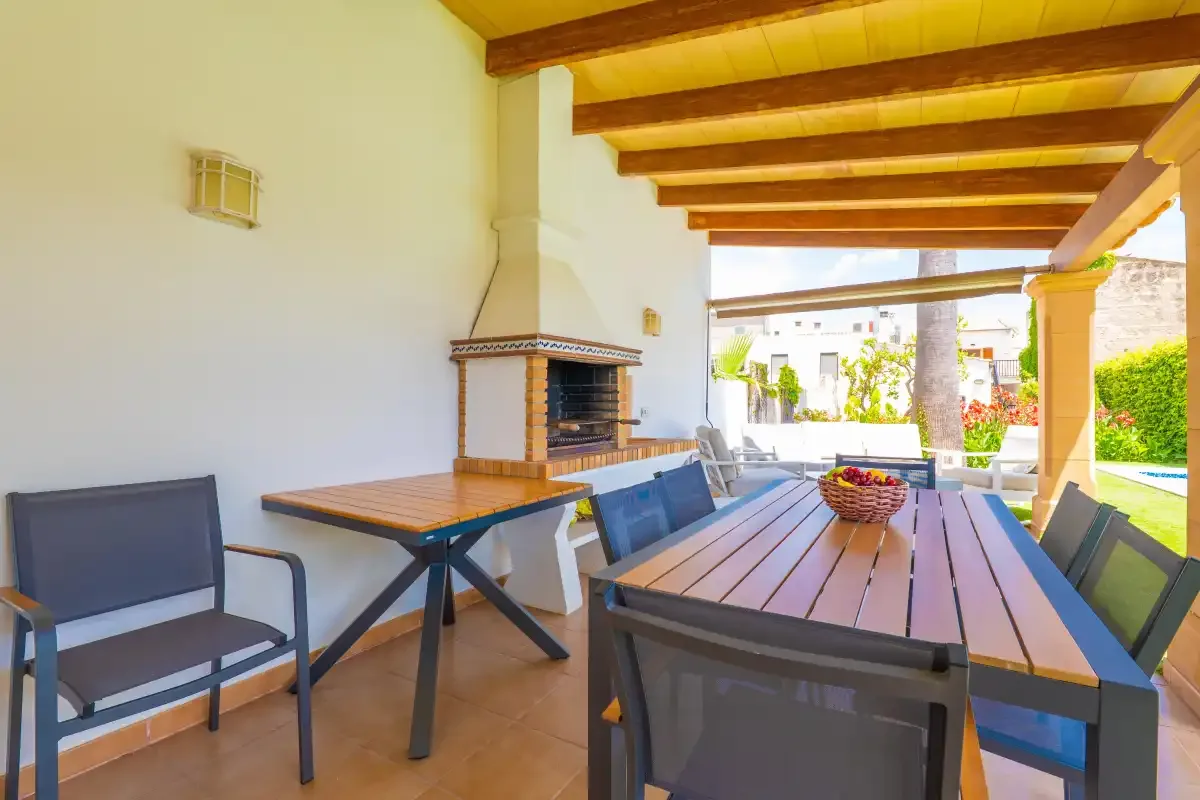 Una zona cubierta para comer al aire libre, con mesa, asientos y una parrilla.