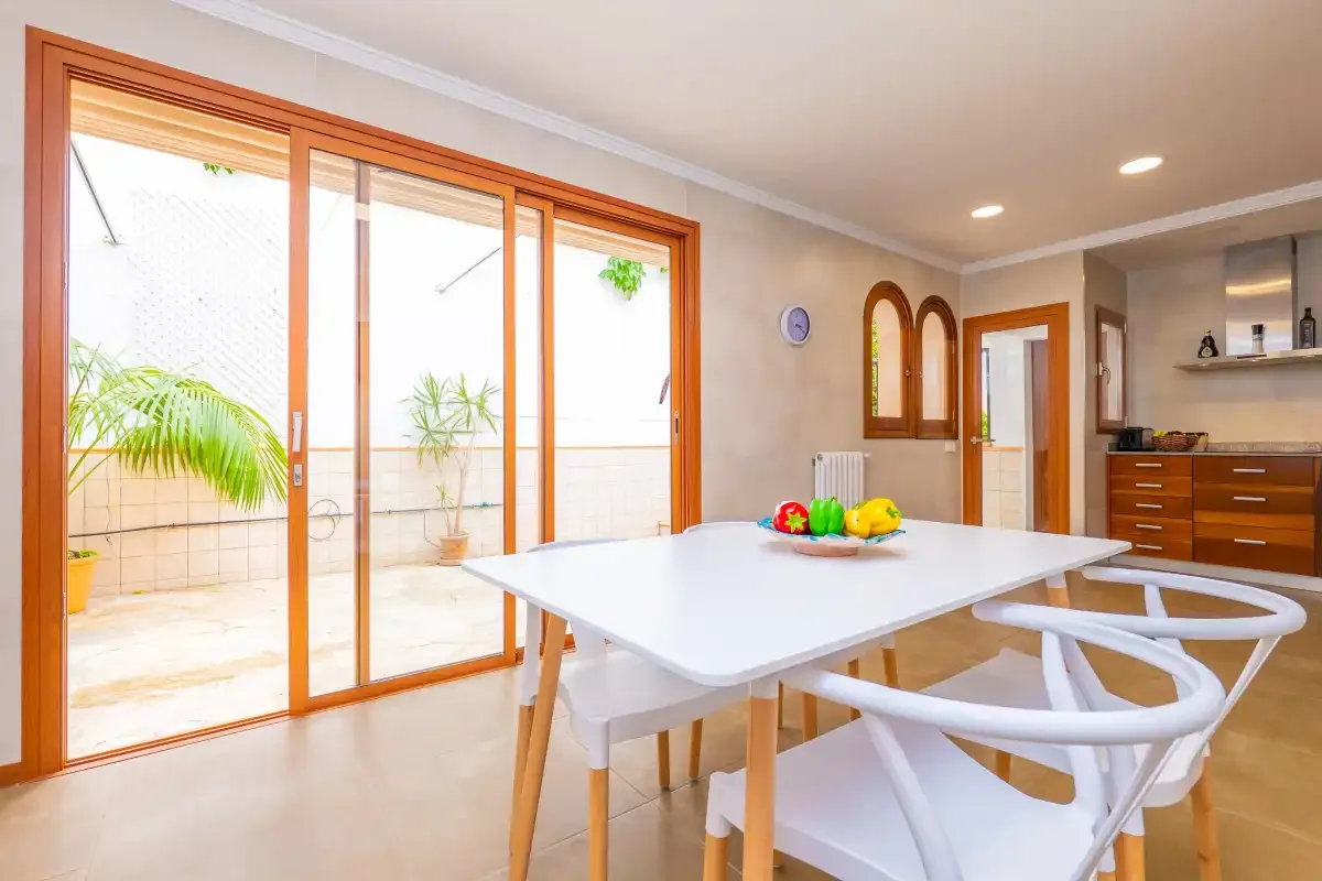 Un comedor luminoso con una mesa junto a grandes puertas de cristal que dan a una terraza.