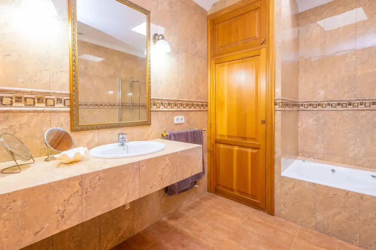 Un baño alicatado con lavabo, espejo y bañera.