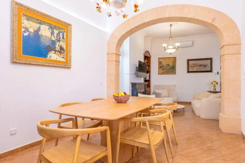 Una zona de comedor con mesa y sillas de madera se abre a una sala de estar mediante un arco.