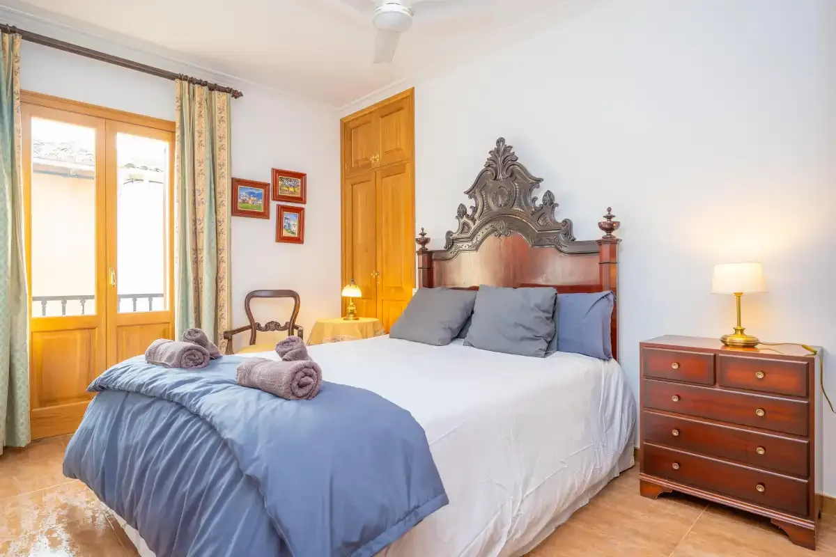 Un dormitorio con cama, cabecero de madera y puertas luminosas al balcón.