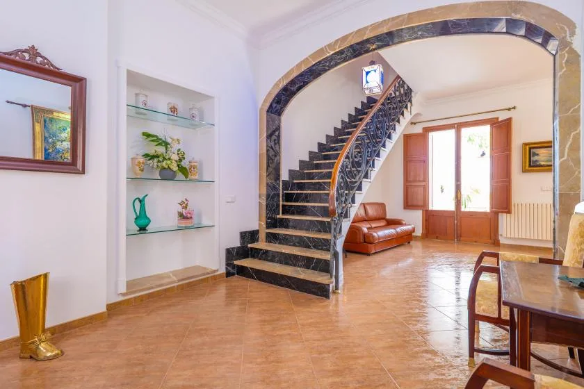 Una sala luminosa con una escalera curva, asientos y una ventana alta.
