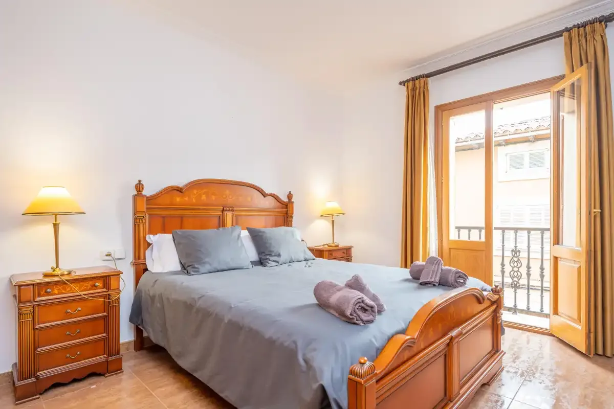 Un dormitorio con una cama de madera, mesillas y una puerta al balcón.