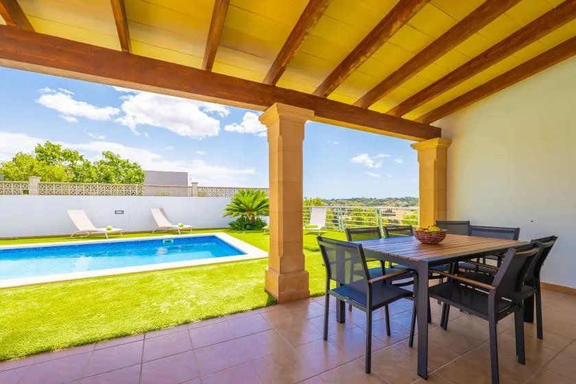 Una zona de comedor exterior cubierta da a una piscina y un césped.