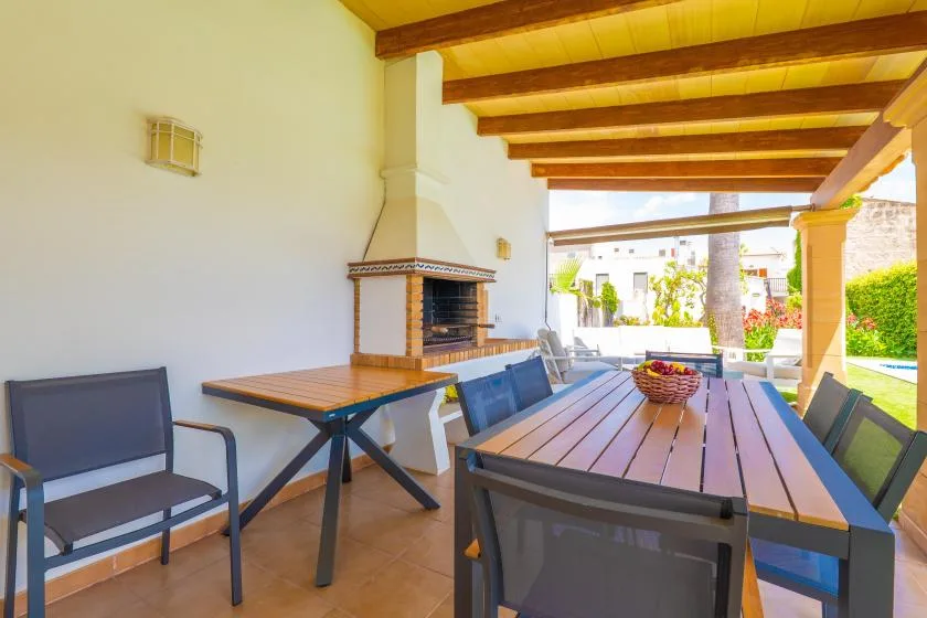Un comedor exterior cubierto con una mesa larga y una barbacoa integrada.